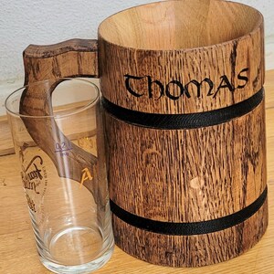 May include: A wooden beer stein with a black band around the top and bottom. The stein is engraved with the name "Thomas".