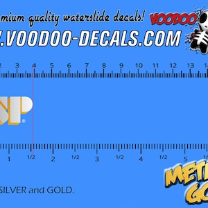 May include: A metallic silver and gold ESP decal on a blue background with a ruler showing a width of approximately 1.5 inches. The image includes the text Premium quality waterslide decals, WWW.VOODOO-DECALS.COM, ESP, and METALLIC GOLD.