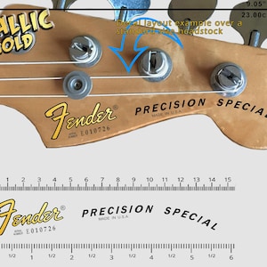 May include: A close-up of a Fender Precision Special bass guitar headstock with a metallic gold decal. The headstock is made of wood and has a natural finish. The decal is gold in colour and features the Fender logo, the words "Precision Special", and the serial number "E010726".
