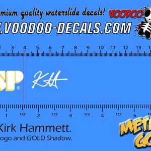 May include: White ESP logo with a gold shadow and Kirk Hammett's signature in white. The text "Metallic Gold" is in gold with a black outline. A ruler is shown for scale.