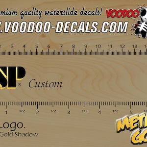 May include: A wooden surface with a ruler in inches and centimeters. The image features the text "Premium quality waterslide decals!" and "WWW.VOODOO-DECALS.COM". It also displays an ESP logo with "Custom" and "ESP Logo. Metallic Gold Shadow."