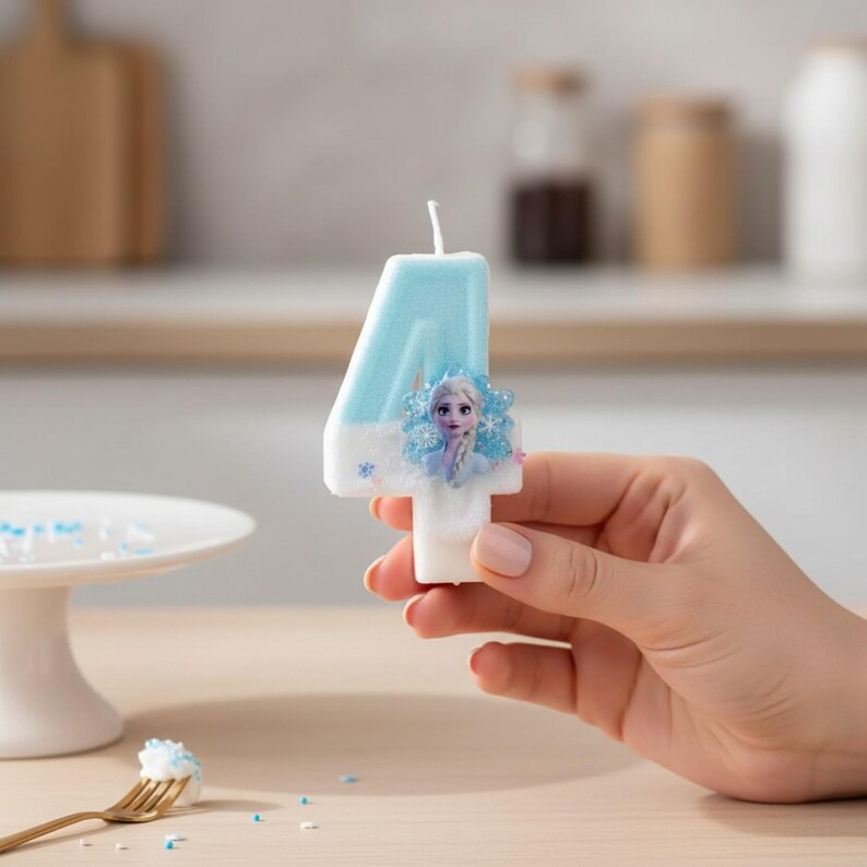May include: A number four birthday candle featuring a light blue and white gradient finish. The candle is decorated with a small, circular graphic of a blonde character with a braid, surrounded by blue snowflake accents on the front surface.