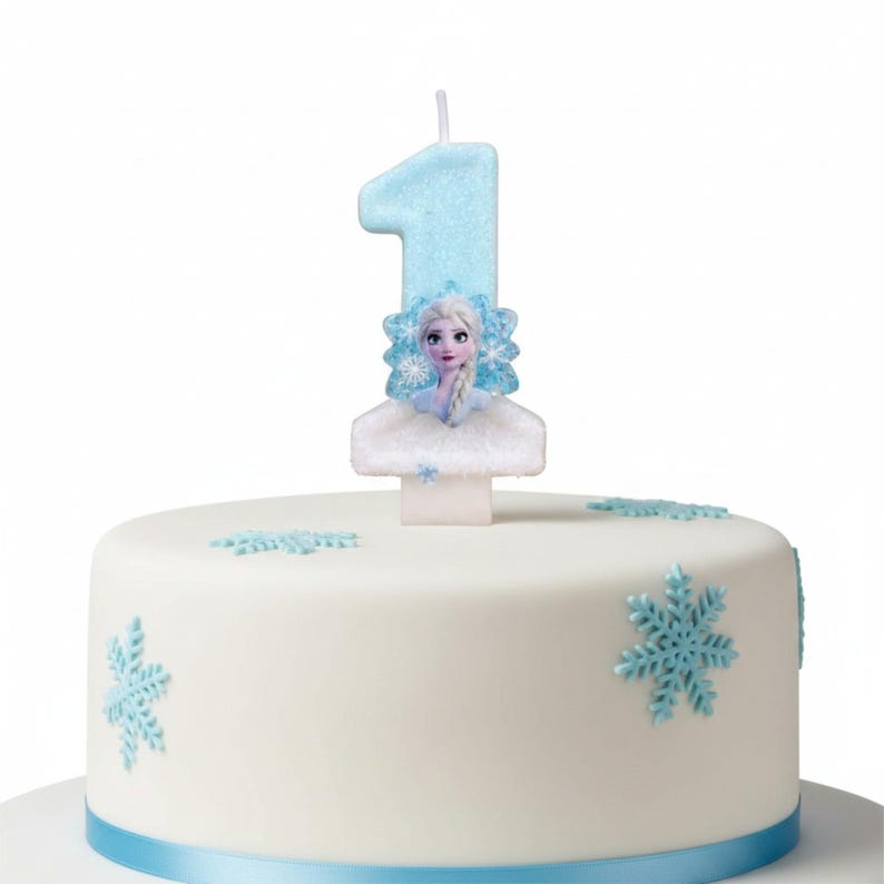 May include: A light blue glittery number one birthday candle featuring a character with blonde hair and a blue snowflake emblem, positioned on top of a white cake decorated with light blue snowflake cutouts and a blue ribbon base.