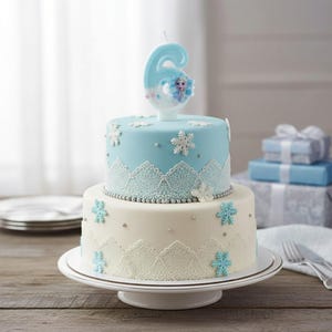 May include: A two-tiered cake with light blue and white frosting, decorated with white lace patterns, silver edible beads, and light blue snowflake cutouts. A number six candle featuring a character illustration sits on the top tier.
