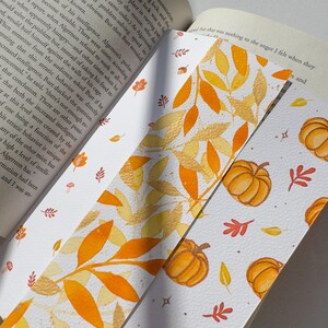 May include: A watercolor bookmark with a fall theme. The bookmark features a pattern of orange and yellow leaves and pumpkins on a white background.
