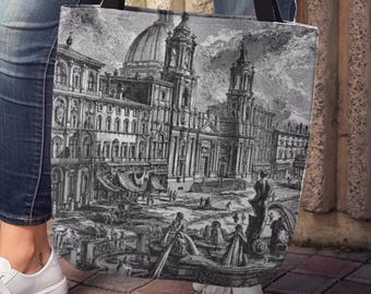 May include: A black and white tote bag featuring a detailed architectural illustration of a European city with a large domed building. The bag has black straps and is held by a person wearing blue jeans and white sneakers.