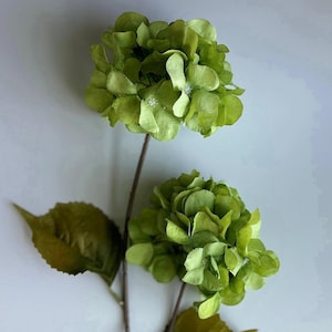 May include: A green hydrangea stem with two large flower heads and a single leaf. The flowers are made of fabric and have a realistic appearance.