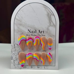 May include: A set of artificial nails with a nude base and colorful rainbow swirl designs. The card reads "Nail Art Best Wishes To You" with sizes XS, S, M, and L. The nails are almond-shaped.