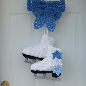 May include: Two white crocheted ice skate ornaments with blue and white snowflake embellishments. The skates are hanging from a blue crocheted butterfly ornament.