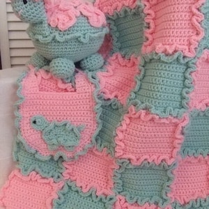 May include: A crocheted baby blanket with a patchwork design in pink and green. The blanket features a crocheted turtle toy.