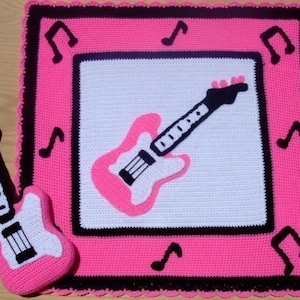 May include: Pink and black crocheted baby blanket with a pink and white guitar design. The blanket has a black border with musical notes.