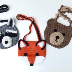 May include: Three crocheted animal-shaped purses with adjustable straps. The purses are a raccoon, a fox, and a bear.