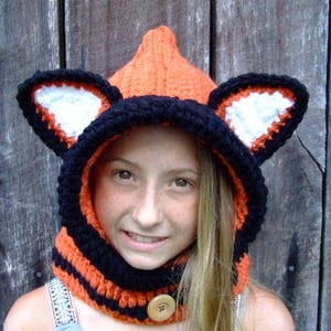 May include: A black and orange striped hooded hat with fox ears. The hat has a white lining inside the ears.