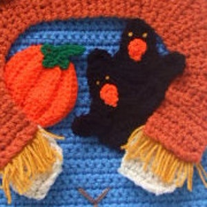 May include: A blue crocheted sweater with a pumpkin, ghost, and orange scarf. The sweater has a brown stitched design on the front.