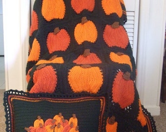 May include: A crocheted throw blanket and pillow featuring a pumpkin design. The blanket is black with orange pumpkins and the pillow is black with a brown wagon filled with orange pumpkins.