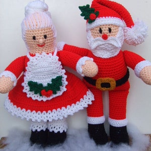 Può includere: Bambole di Babbo Natale e la signora Claus all'uncinetto. Babbo Natale indossa un abito rosso con bordi bianchi e una cintura nera. La signora Claus indossa un vestito rosso con un grembiule bianco e un bordo di pizzo bianco.