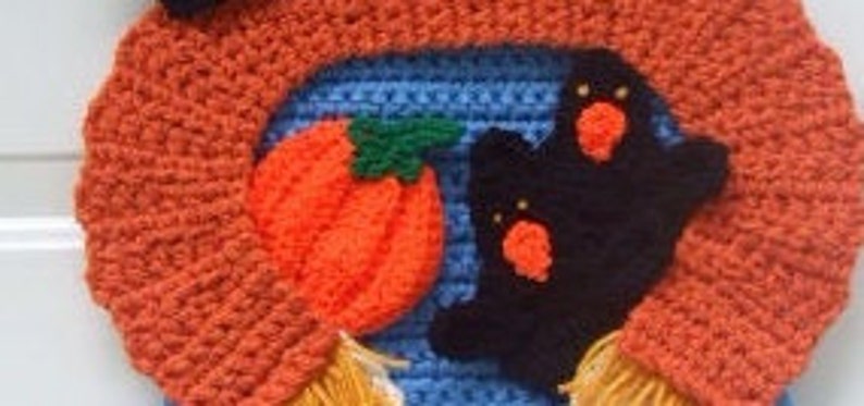 May include: A crocheted Halloween wreath with orange, blue, and black yarn. The wreath features a pumpkin, two ghosts, and a witch's hat.