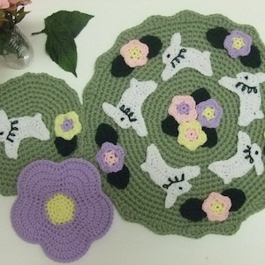 May include: Set of three crocheted green and white coasters with a flower and bunny design. The coasters are round and have a scalloped edge.
