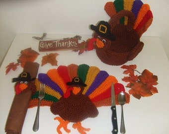 Puede incluir: Porta tarjetas de lugar y anillos de servilleta de pavo hechos a crochet para el Día de Acción de Gracias. El porta tarjetas de lugar de pavo tiene un cuerpo marrón, una cola colorida y un sombrero negro. El anillo de servilleta tiene un cuerpo marrón y un sombrero negro. El letrero dice "Give Thanks".