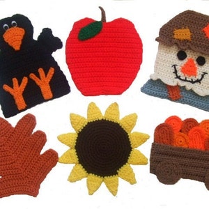 May include: A set of seven crocheted fall-themed decorations, including a black crow, a red apple, a scarecrow, a brown leaf, a yellow sunflower, and a brown wagon with orange logs.