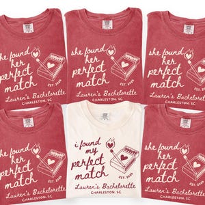 May include: Five short-sleeved t-shirts in crimson and ivory colors. The shirts feature a graphic of a matchbox with a heart and a lit match, with the text "she found her perfect match" or "i found my perfect match," "EST. 2026," "Lauren's Bachelorette," and "CHARLESTON, SC."