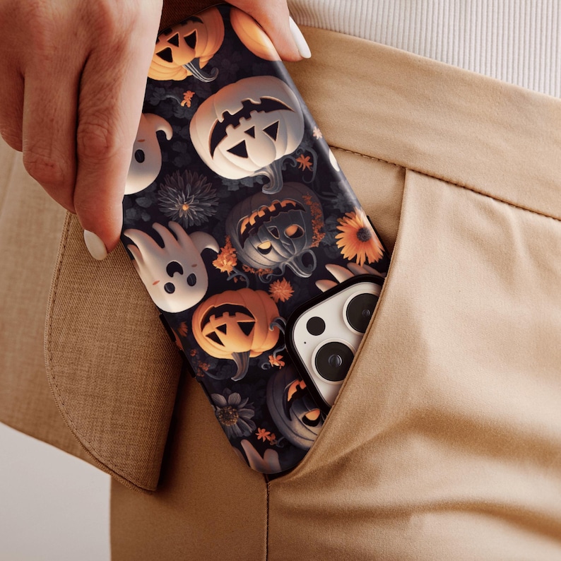 May include: A black phone case with a Halloween theme. The case features a pattern of pumpkins, ghosts, and flowers. The phone case is in a pocket of a pair of brown pants.