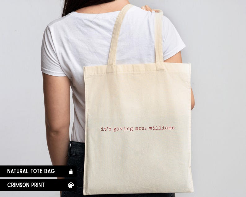 K&ouml;nnte beinhalten: Eine naturfarbene Stofftasche mit dem Text "it's giving mrs. williams", der in einer karmesinroten Schreibmaschinenschrift aufgedruckt ist. Die Tasche hat zwei Schulterriemen und eine rechteckige Form f&uuml;r ein schlichtes und funktionales Design.