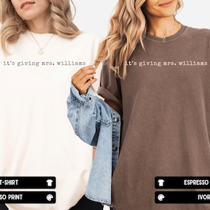 K&ouml;nnte beinhalten: Zwei kurz&auml;rmelige T-Shirts mit Rundhalsausschnitt, eines in Elfenbein mit espressofarbenem Text und eines in Espresso mit elfenbeinfarbenem Text. Beide T-Shirts tragen den Schriftzug "it's giving mrs. williams" in einer Schreibmaschinen-Schriftart.