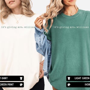K&ouml;nnte beinhalten: Zwei kurz&auml;rmelige T-Shirts mit Rundhalsausschnitt, eines in Elfenbein und eines in Hellgr&uuml;n. Beide Shirts tragen den Schriftzug "it's giving mrs. williams" auf der Brust in einer Schreibmaschinen-Schriftart. Das elfenbeinfarbene Shirt hat hellgr&uuml;nen Text, das hellgr&uuml;ne Shirt elfenbeinfarbenen Text.