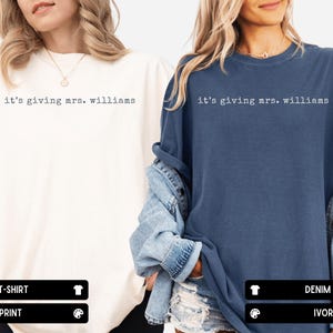 K&ouml;nnte beinhalten: Zwei kurz&auml;rmelige T-Shirts mit Rundhalsausschnitt, eines in Elfenbein und eines in Denimblau, beide mit dem schwarzen Schriftzug "it's giving mrs. williams" auf der Brust. Die T-Shirts haben eine lockere Passform mit klassischem Ausschnitt und Saum.