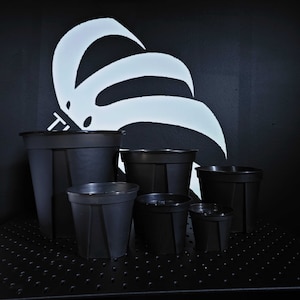 May include: A set of six black plastic plant pots of varying sizes. The pots are arranged in a pyramid shape on a black surface.