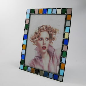 May include: A colorful picture frame with a mosaic of blue, green, orange, yellow, and pink glass squares. The frame is holding a photo of a woman with blonde hair.