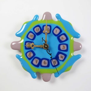 May include: A blue, green, and purple glass clock with a gold-colored face and black hands. The clock is shaped like a melting blob.