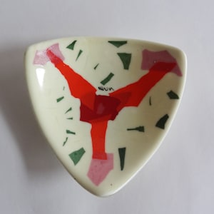 May include: A white triangular ceramic dish with a red, green, and pink abstract design. The dish has a glossy finish and the word "moon" is written in black on the surface.