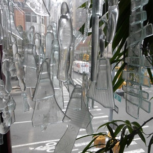 以下が含まれることがあります： 透明なガラスの風鈴が、紐からぶら下がっている様子のクローズアップ。風鈴は、街の通りが見える窓の前に吊るされています。