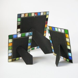 Op de afbeelding: Drie decoratieve fotolijsten met kleurrijke moza&iuml;ektegels. De frames hebben zwarte achterkanten en standaards. De moza&iuml;ektegels zijn in tinten blauw, groen, oranje, geel en wit. Verschillende maten.
