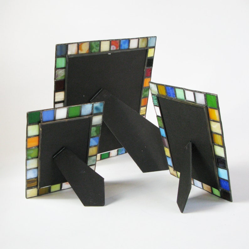 Op de afbeelding: Drie decoratieve fotolijsten met kleurrijke moza&iuml;ektegels. De frames hebben zwarte achterkanten en standaards. De moza&iuml;ektegels zijn in tinten blauw, groen, oranje, geel en wit. Verschillende maten.