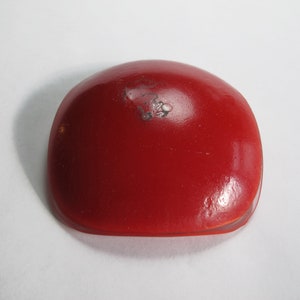 May include: A red, round, ceramic dish with a slightly domed top. The dish is smooth and glossy.