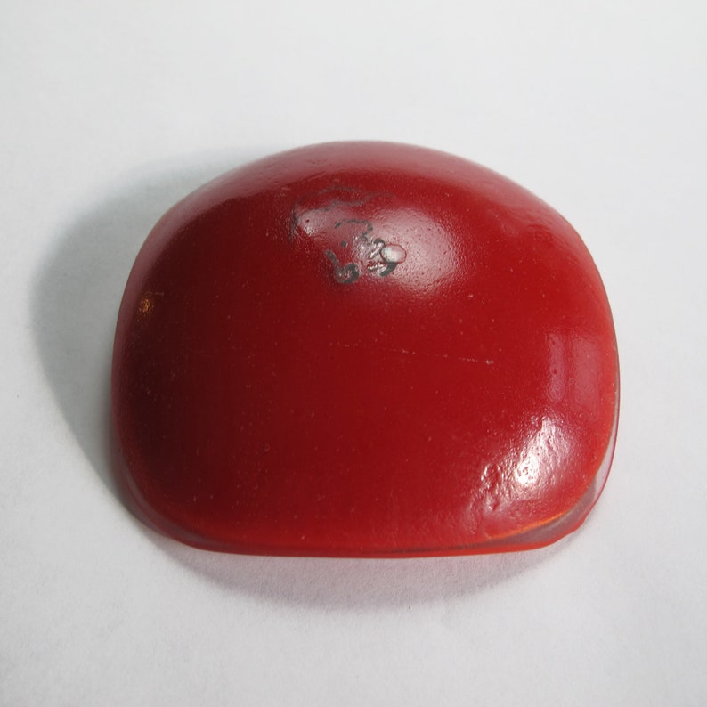 May include: A red, round, ceramic dish with a slightly domed top. The dish is smooth and glossy.
