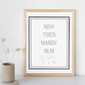 May include: A black and white framed print with the text "NOW THEN MARDY BUM" and a simple line drawing of two hands holding a clothesline.