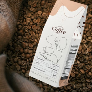 Può includere: Un sacchetto di caffè bianco con un design minimalista che presenta un disegno a linea di una persona che beve caffè. Il sacchetto è etichettato "every morning Coffee" e include dettagli sulle note di degustazione del caffè, la regione, il livello di tostatura, i metodi di preparazione e la dimensione. Il sacchetto è su un mucchio di chicchi di caffè.