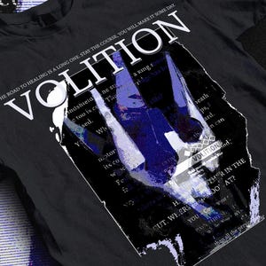 May include: Black t-shirt with the word "VOLITION" in white, featuring a distressed graphic with blue and white accents. The shirt includes text that reads "THE ROAD TO HEALING IS A LONG ONE. STAY THE COURSE, YOU WILL MAKE IT SOME DAY."