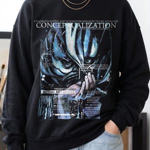 Puede incluir: Una sudadera negra de cuello redondo con un estampado gráfico de un rostro estilizado en azul y negro con ojos grandes. El texto dice: CONGRATUALTIONS, YOU'VE SOMEHOW MANAGED TO FAIL AT FAILING CONCEPTUALIZATION, THOUGHT COMPLETE, ACTUAL ART DEGREE.
