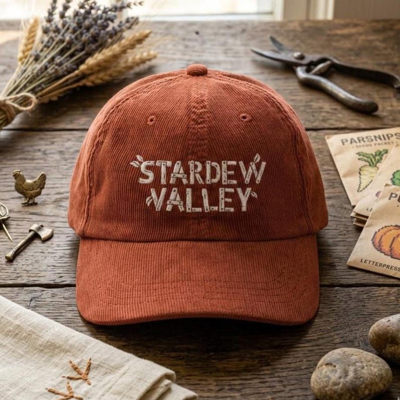 Sorgu başarılı

Gemini şunu dedi:

A rust-colored, corduroy baseball cap sits centered on a rustic wooden table. The front features "STARDEW VALLEY" embroidered in white, blocky letters with small leaf accents. The cap has a classic 6-panel structure and a curved brim.