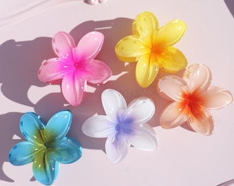 May include: Six colorful plastic flower hair clips on a pink tray. The clips are in shades of pink, yellow, blue, orange, and white.