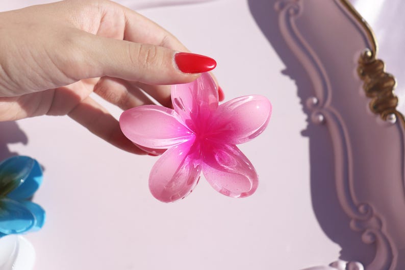 May include: A pink and white plastic flower with five petals. The flower is translucent and has a glossy finish.