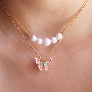 May include: A gold chain necklace with a delicate butterfly pendant and a row of five white pearls.