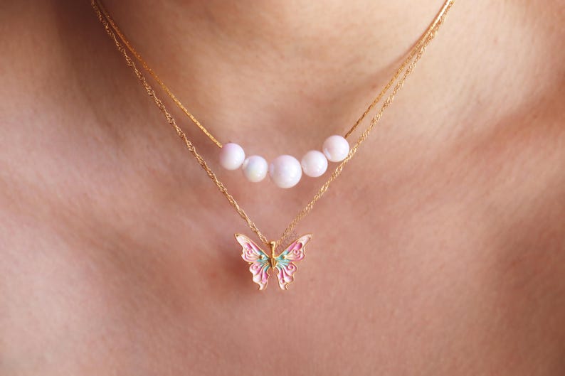 May include: A gold chain necklace with a delicate butterfly pendant and a row of five white pearls.