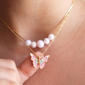 May include: A gold chain necklace with a row of five white pearls and a pink and green butterfly pendant.