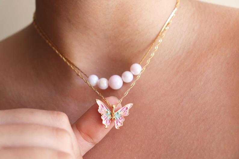 May include: A gold chain necklace with a row of five white pearls and a pink and green butterfly pendant.